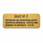 Златиста гравирана индустриална табелка с надпис „HAAS VF-2“ и технически спецификации на вертикален CNC обработващ център