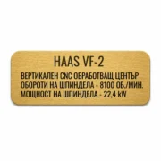 Златиста гравирана индустриална табелка с надпис „HAAS VF-2“ и технически спецификации на вертикален CNC обработващ център